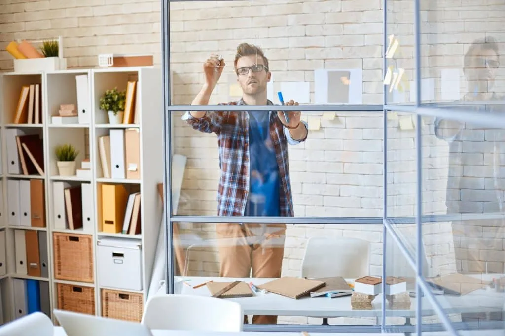 A man writing on a glass board in an office