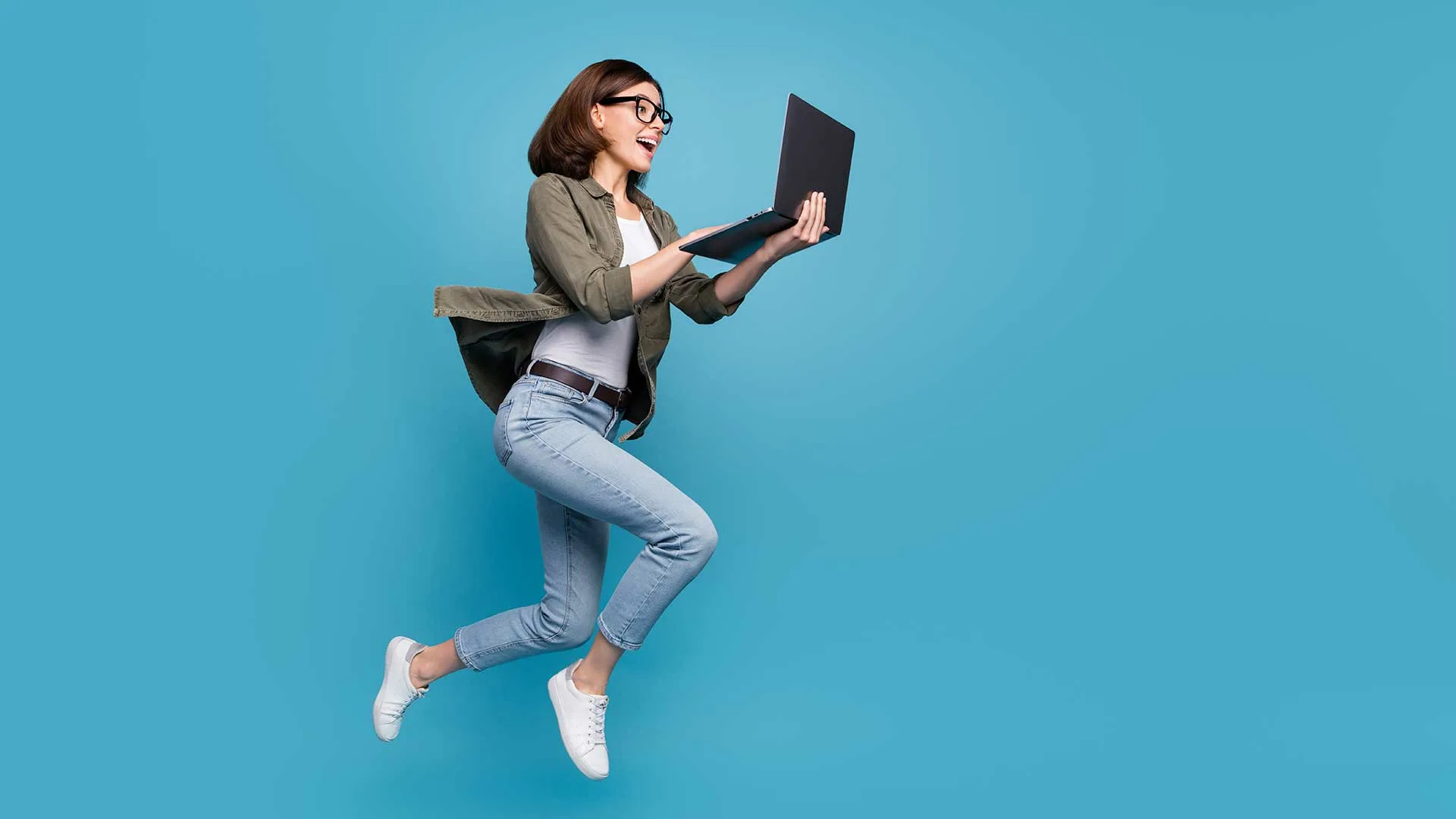 A woman jumping in the air while holding an open laptop
