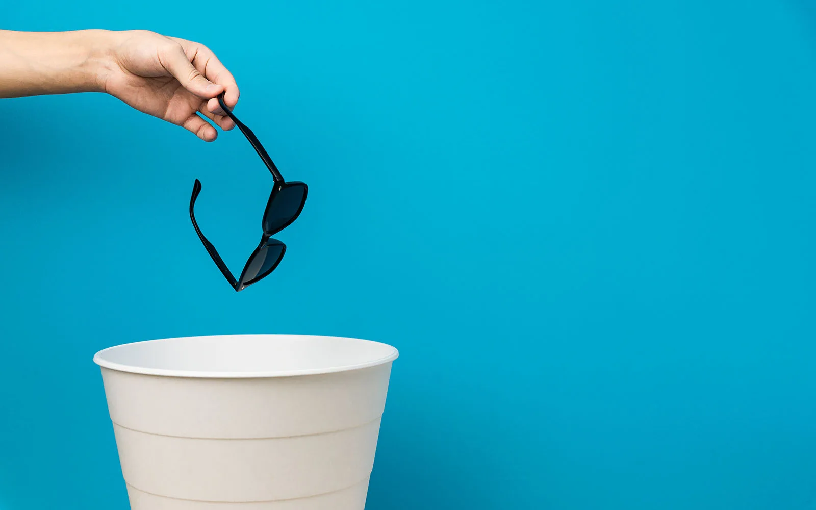 A person dropping sunglasses into a bucket