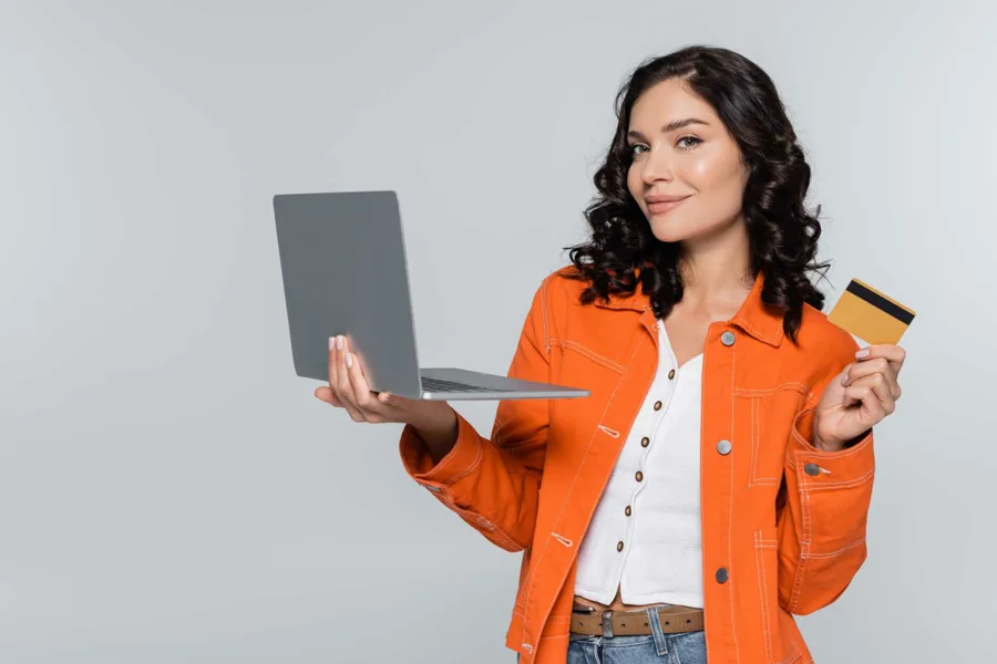 A smiling woman holding an open laptop and a credit card