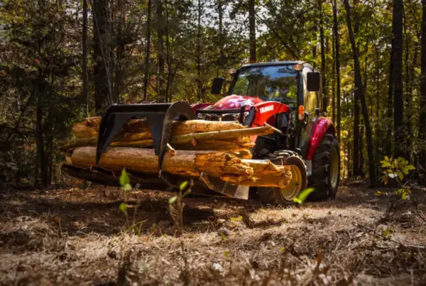 A red yanmar tractor in a forest clearing holding logs in it's levered jaw