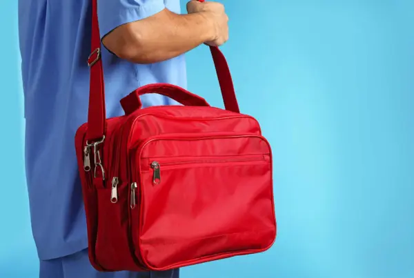 A male nurse holding a red medical supply bag